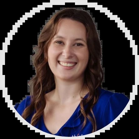 Professional headshot of a smiling woman with long brown wavy hair wearing a blue v-neck top