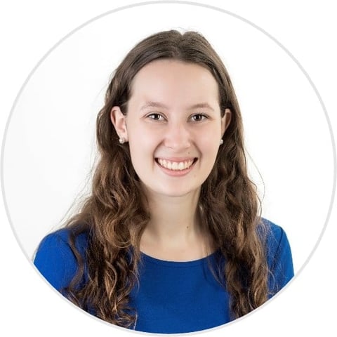 Young woman with long brown wavy hair wearing a blue shirt, smiling at the camera in a circular portrait photo