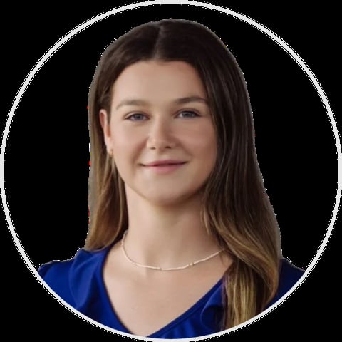 Portrait of a young woman with long brown hair wearing a blue top and silver necklace against a dark background
